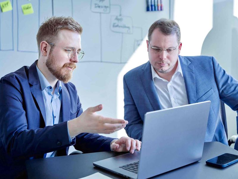 Team Starter ab 990 Euro: zwei Kollegen im Gespräch am Laptop im Büro