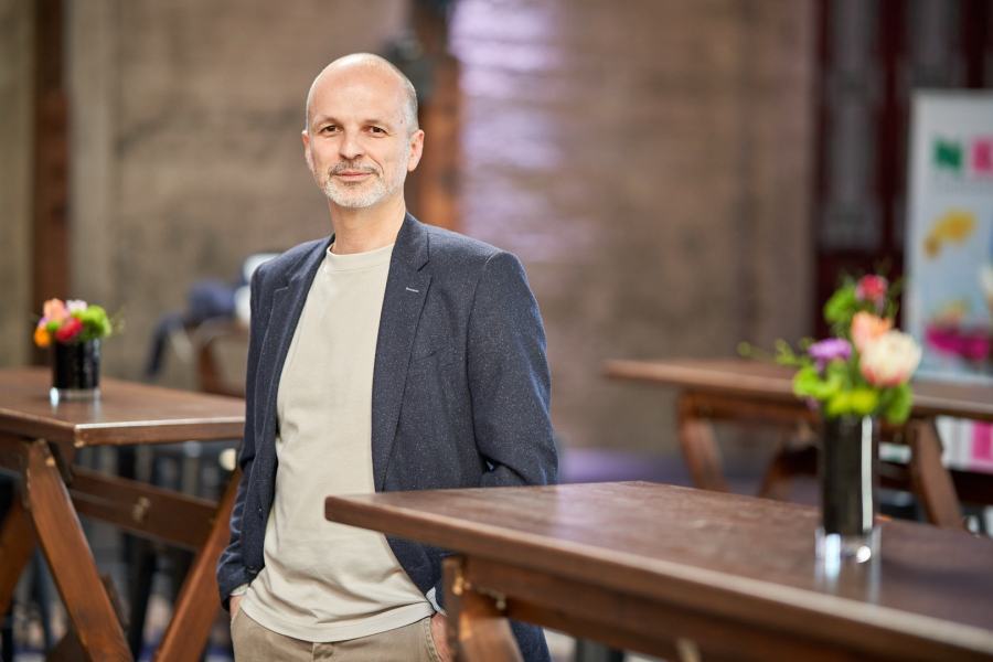 Vassilios Katsogridakis im blauen Blazer an der langen Tischreihe eines Eventraums