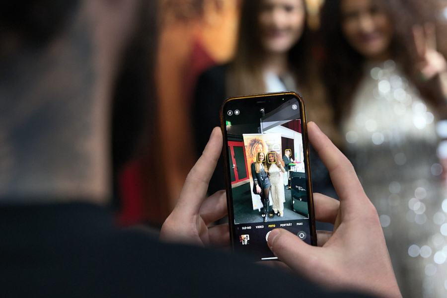 Fotograf richtet Smartphone auf zwei feiernde Frauen bei Friseur-Event